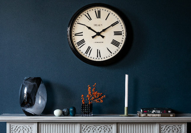 A Heal's analogue clock over a carefully styled mantelpiece