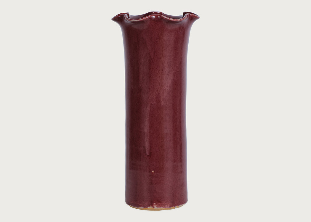 A tall, flared ceramic vase with a glossy deep burgundy glaze, shown against a plain light gray background.