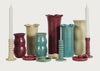 A collection of ceramic vases and candlestick holders in multiple colors including teal, burgundy, beige, and green, arranged on a light gray background.