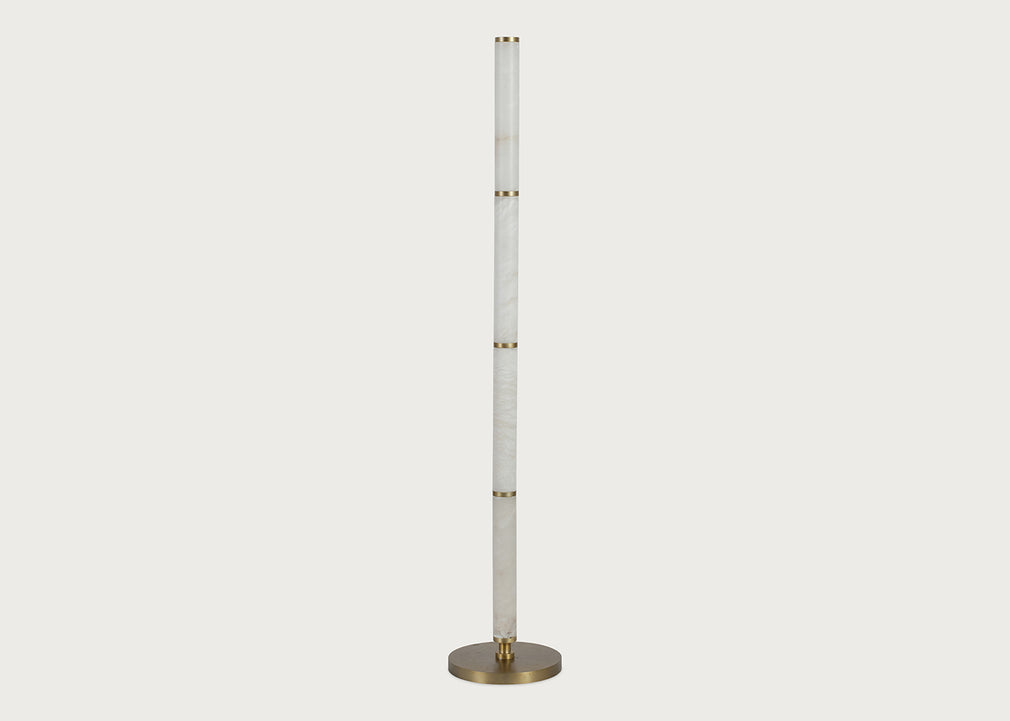 A modern floor lamp featuring a tall, slender alabaster column with gold-toned metal accents and a circular brushed brass base, shown against a solid light gray background.