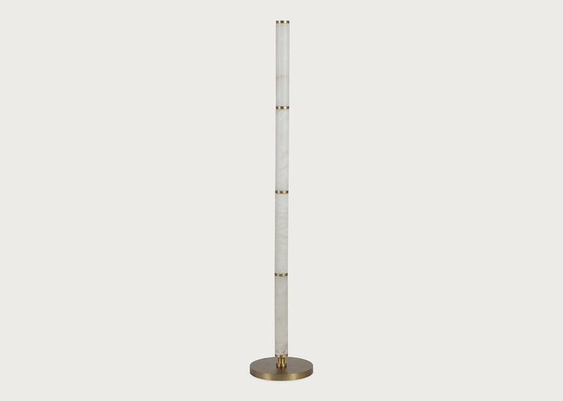 A modern floor lamp featuring a tall, slender alabaster column with gold-toned metal accents and a circular brushed brass base, shown against a solid light gray background.
