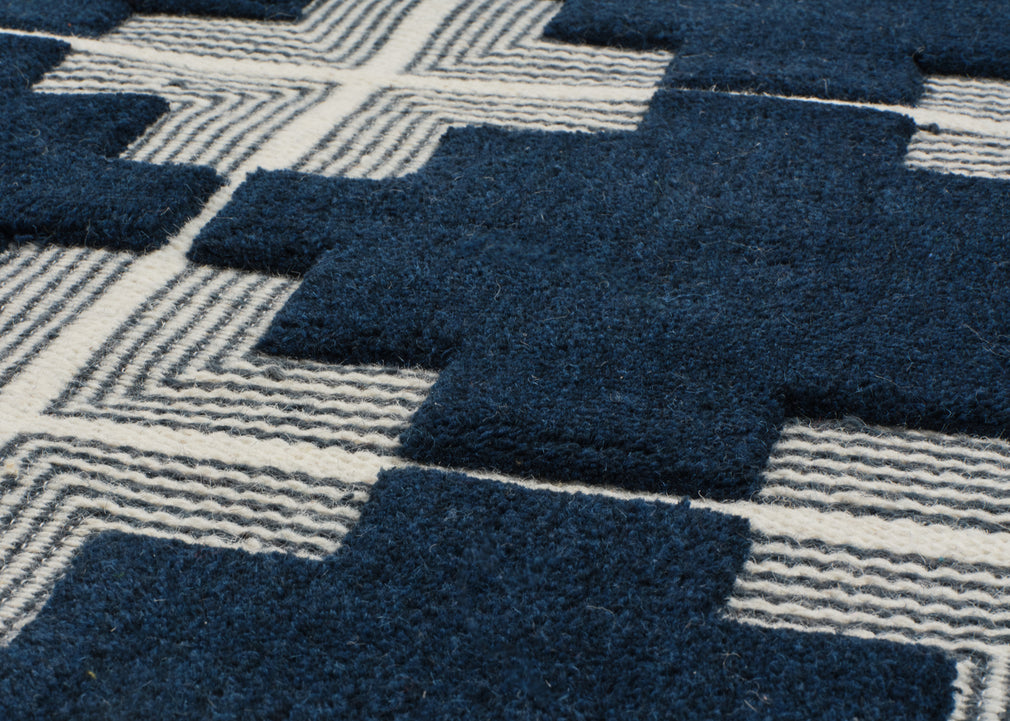 Close-up of a textured area rug with a geometric pattern of dark navy blue blocks and cream-colored wavy lines.