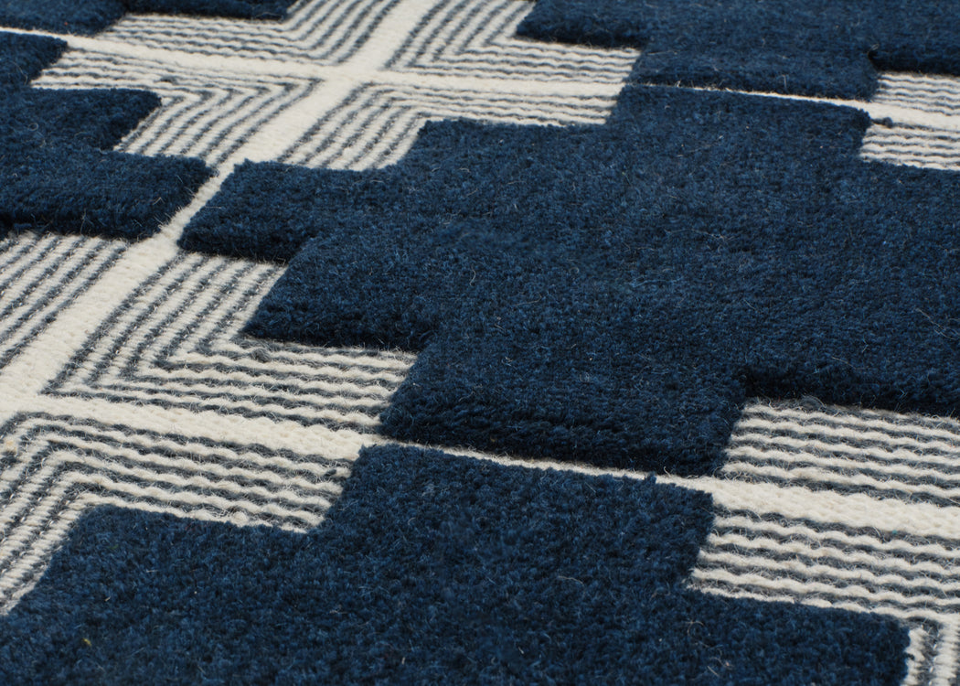 Close-up of a textured area rug with a geometric pattern of dark navy blue blocks and cream-colored wavy lines.