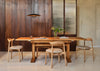 A modern dining room setup featuring a rectangular wooden dining table with four matching wooden chairs with light beige upholstered seats, set against a dark wood-paneled wall.