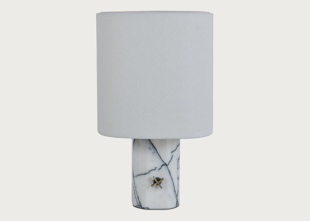 A table lamp with a cylindrical white fabric shade and a white marble base featuring dark veining and a small brass accent.