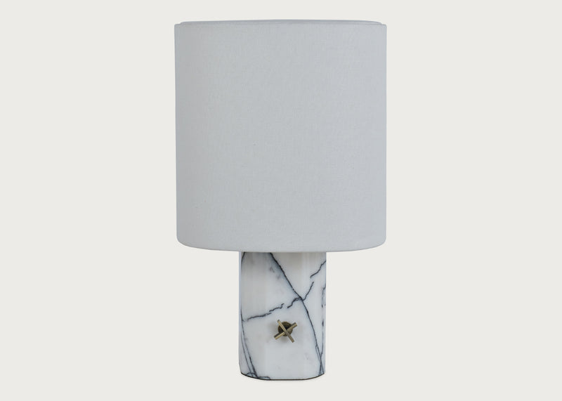 A table lamp with a cylindrical white fabric shade and a white marble base featuring dark veining and a small brass accent.
