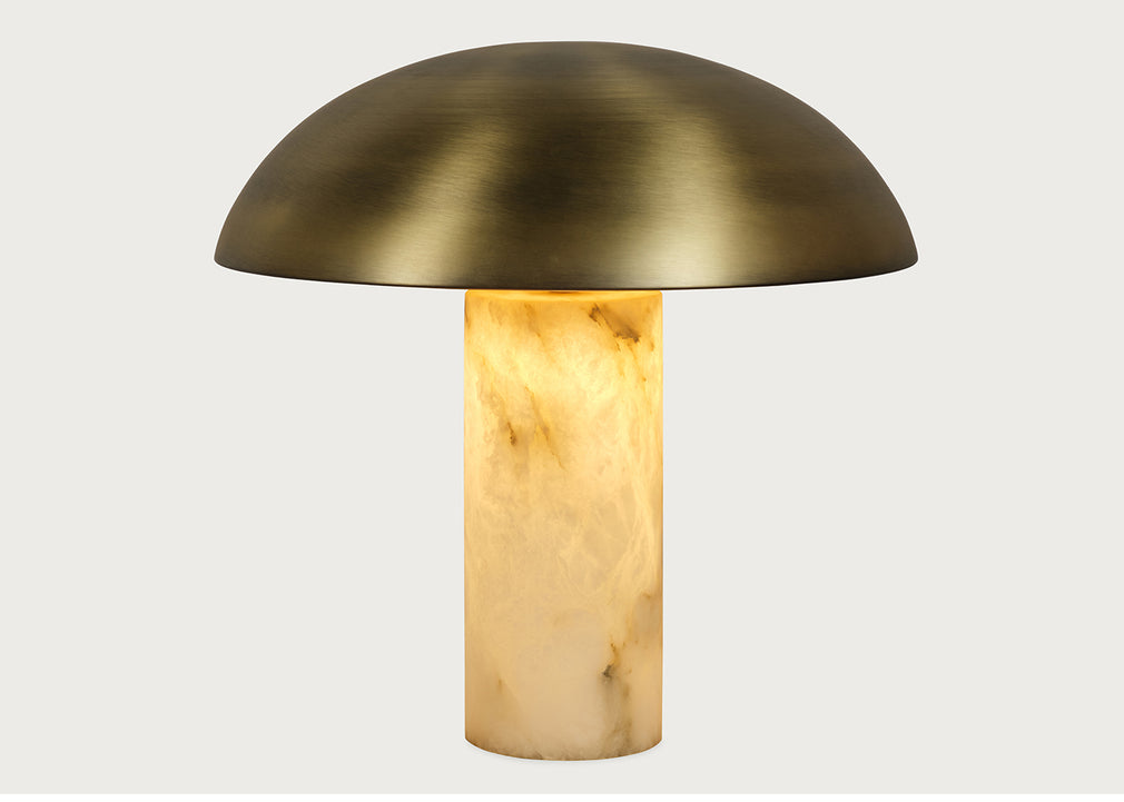 A mushroom-shaped table lamp with a brushed brass dome shade and a glowing warm alabaster stone column base, shown against a light gray background.