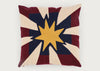 A square decorative throw pillow featuring a stylized starburst design with a central yellow star, navy blue center, and alternating cream and burgundy rays, shown against a plain light gray background.