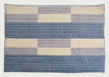 A rectangular quilted blanket with a geometric striped pattern in shades of blue, gray, and cream, displayed flat against a plain white background.